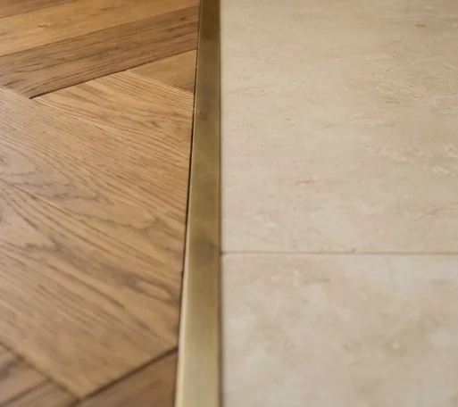 Brass transition between oak flooring and light stone tiles