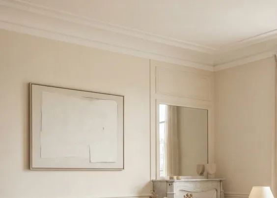 Cream painted wall with classic panel mouldings, a framed artwork and a fireplace mirror