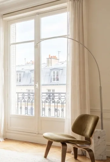 Tall French window with linen curtains and a lounge chair in warm daylight